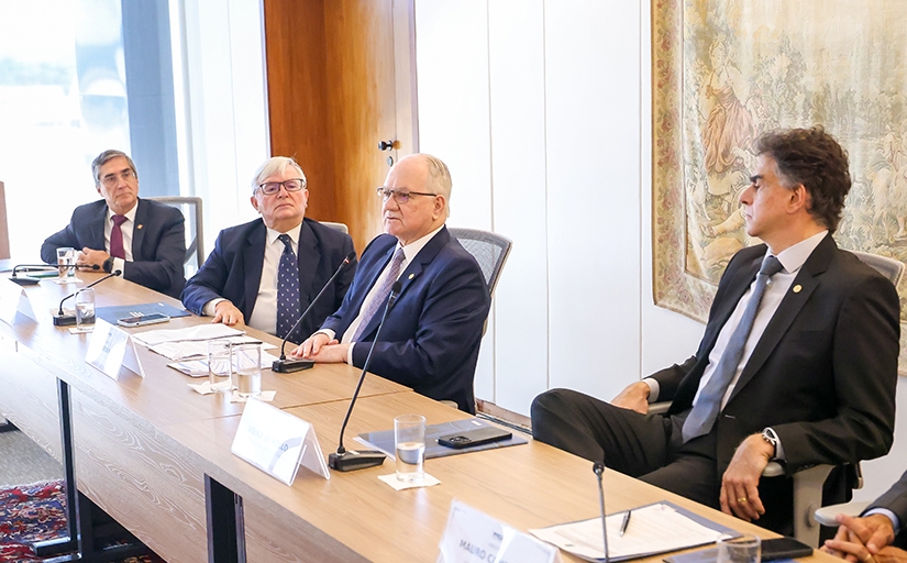 Quatro homens de terno sentados à mesa de um evento