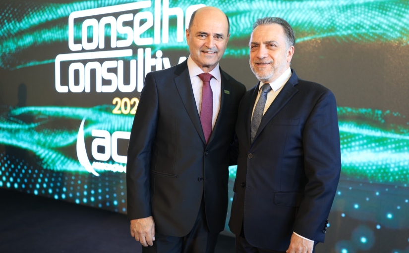 Dois homens de terno posam para a foto em frente a um telão digital