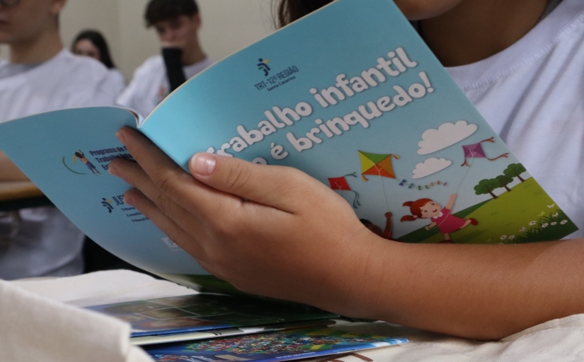 Imagem em close de um jovem segurando uma cartilha com o nome Trabalho infantil não é brinquedo