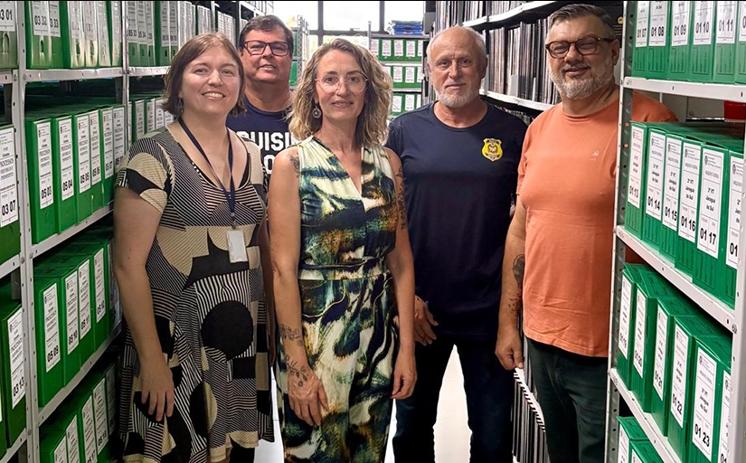 Três homens e duas mulheres posando para foto em meio a estantes com caixas de arquivos