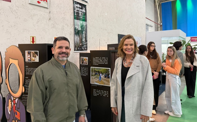 Um homem e uma mulher estão em pé, em uma exposição de fotografia, posando para a foto