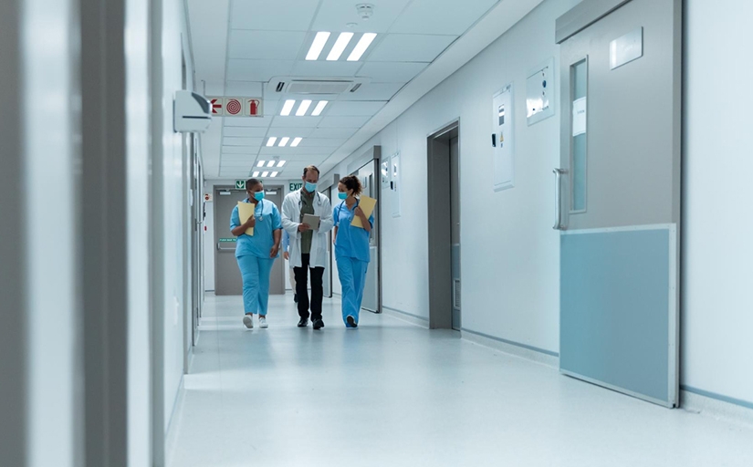 Corredor de hospital com três pessoas vestindo jaleco médico.