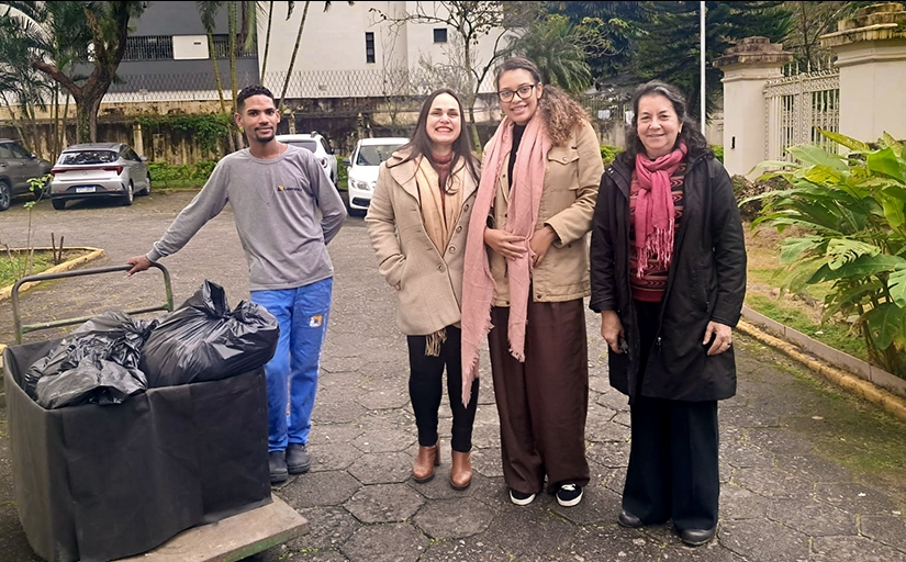 Três mulheres e um rapaz posam para foto ao lado de um carrinho de transporte com sacos pretos