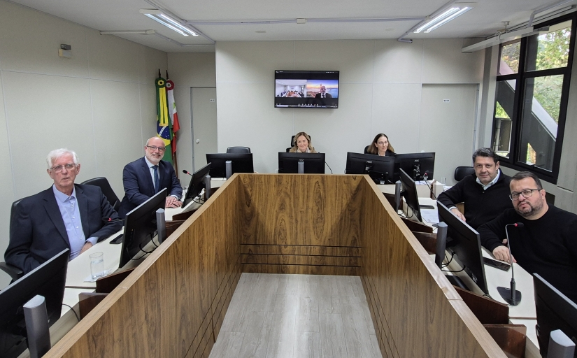 Quatro homens e duas mulheres posam para a foto, sentados ao redor de uma mesa em formato de U