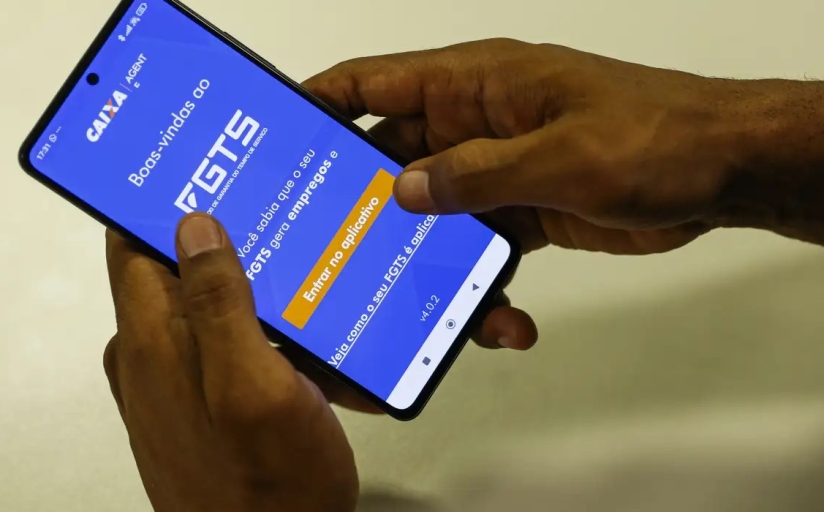 duas mãos segurando um celular, com o aplicativo da "caixa" aberto, tendo o fundo azul, com um letreiro em branco escrito "FGTS"
