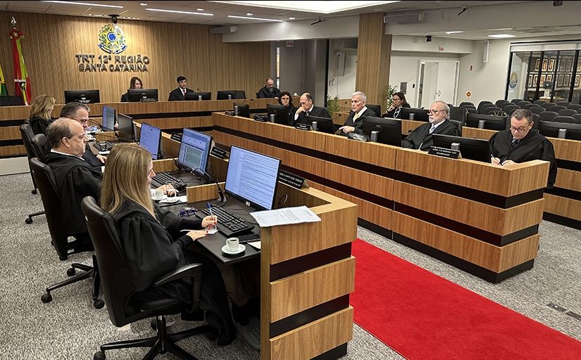 13 pessoas vestem roupas pretas, todas sentadas em torno de duas bancadas laterais e uma central, formando a letra U