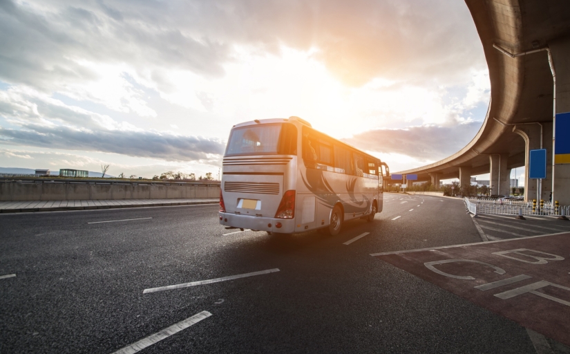 onibus branco, em uma estrada, com o céu de fundo possuindo sol e nuvens