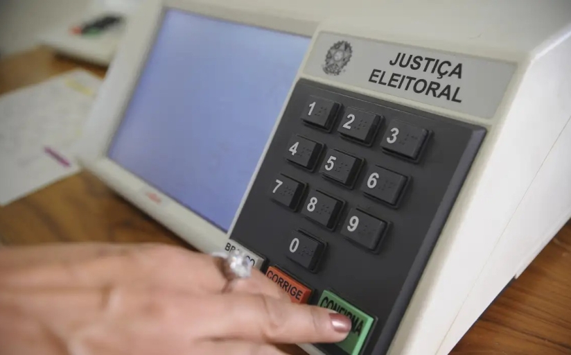 Mão aperta tecla de uma urna eletrônica
