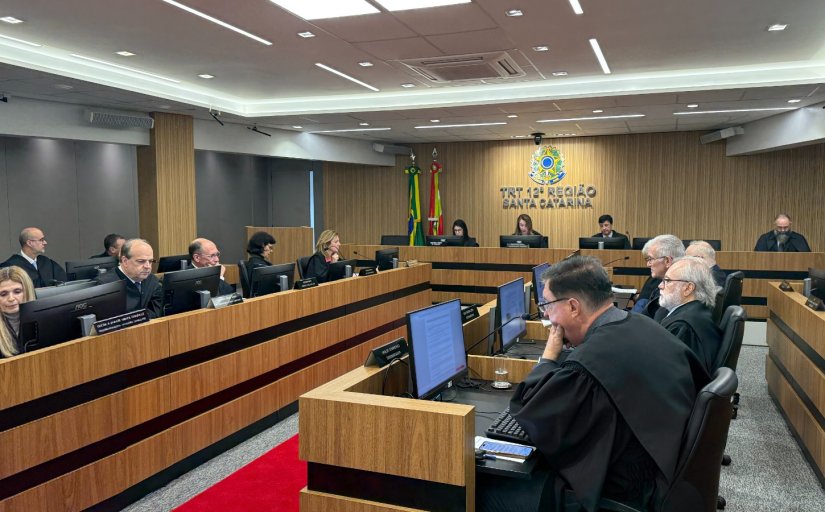 Trezes pessoas vestindo toga sentadas em fileiras de bancadas de madeira, em uma sala de julgamento