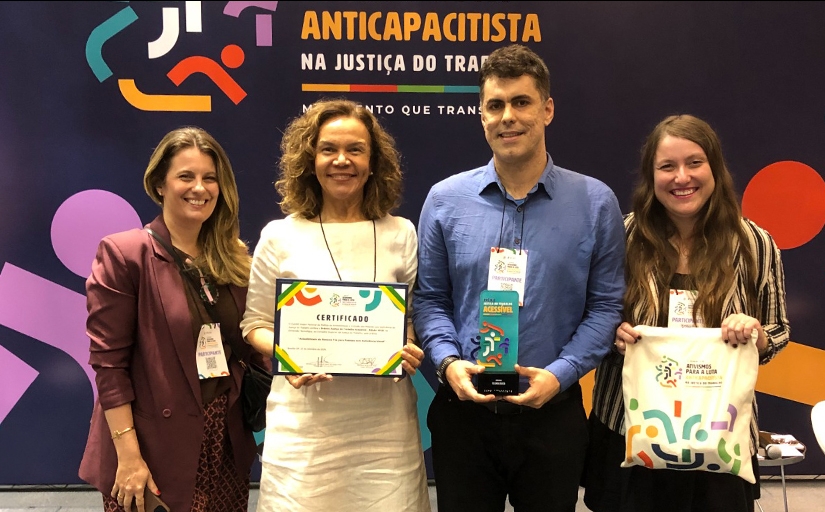 Três mulheres e um homem estão em pé, posando para a foto, com um certificado nas mãos