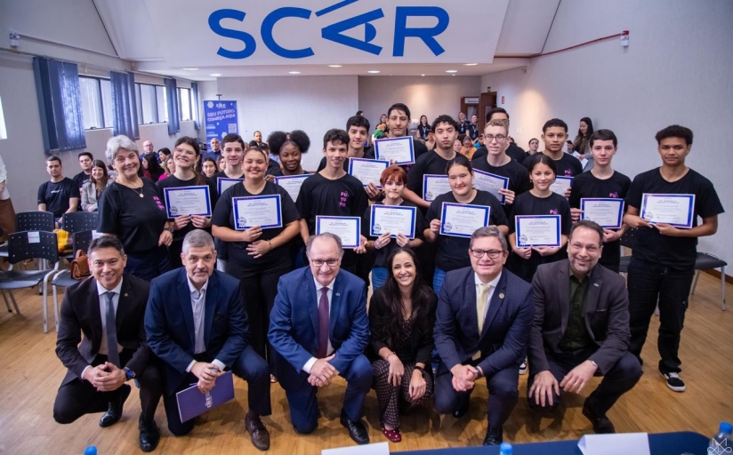Grupo de jovens recebe certificados durante evento, acompanhado por autoridades e organizadores.