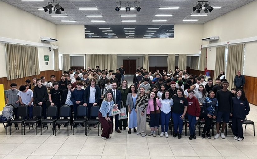 Cerca de cem jovens e adolescentes e outros quatro adultos posam para foto, de pé, em um amplo auditório