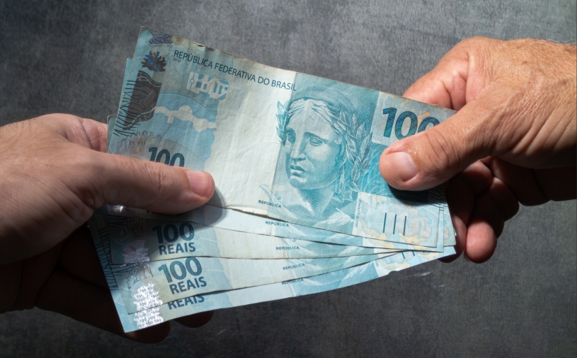 Mão recebe cédulas de 100 reais de outra mão