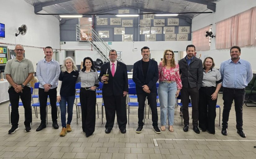 Seis homens e quatro mulheres posam para foto, lado a lado, dentro de uma sala ampla e com pé direito alto. Uma das pessoas, de terno, segura uma cuia de chimarrão