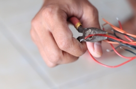 Foto em detalhe de uma mão segurando um alicate e cortando fios