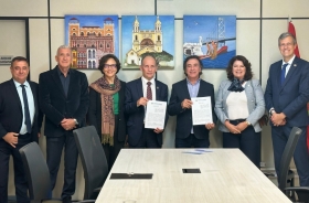 Duas mulheres e cinco homens estão em pé, sorrindo e posando para a foto, em uma sala de reuniões com quadros coloridos na parede