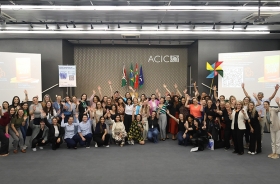 Grupo de pessoas reunidas e sorrindo em auditório da ACIC, com bandeiras ao fundo e clima de celebração.