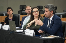 Palestrantes participam de mesa-redonda em auditório, com notebooks e microfones sobre a mesa.