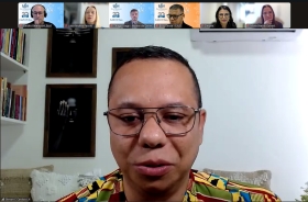 Rosto de um homem negro, de óculos, cabelo curto, falando em uma videoconferência