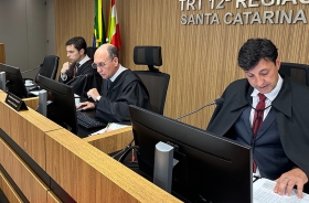 Fotografia de três homens sentados à bancada, analisando processos no plenário do TRT-SC
