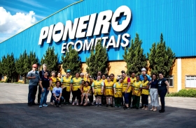Foto de um grupo de pessoas, algumas com colete amarelo, em pé, em frente a uma empresa com o nome Pioneiro Ecometais