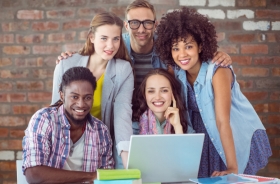 Fotografia ilustrativa de cinco pessoas sorrindo para a foto, três mulheres e dois homens. À frente deles existem livros e um notebook.