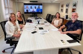 Grupo de pessoas sentadas ao redor de uma mesa branca posam para a foto