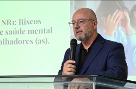 Homem vestindo terno e usando óculos fala ao microfone