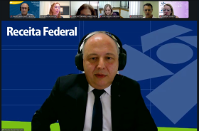 Print de tela de um homem grisalho de terno e gravata fazendo uma palestra por videoconferência