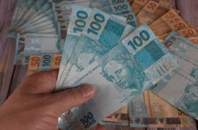 Foto de uma mão masculina segurando notas de cem reais.