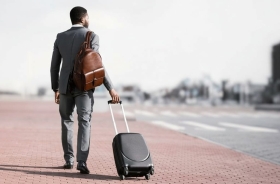 Fotografia ilustrativa de homem negro de terno claro e malas olhando para o horizonte distante