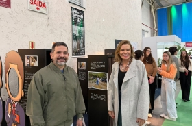 Um homem e uma mulher estão em pé, em uma exposição de fotografia, posando para a foto