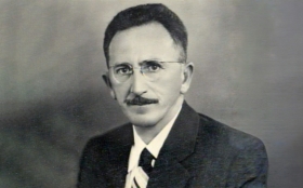 Foto preta e branca de um homem de óculos e bigode
