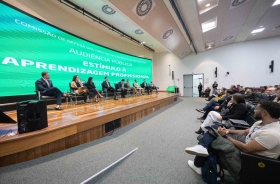 Fotografia de auditório com painel sobre aprendizagem profissional e plateia assistindo.