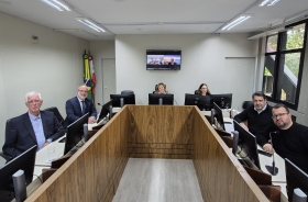 Quatro homens e duas mulheres posam para a foto, sentados ao redor de uma mesa em formato de U