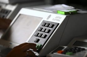 Urna eletrônica branca, com uma digitando um número