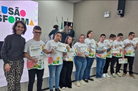 Mulher posa com 10 jovens lado a lado. Todos eles exibem um certificado.
