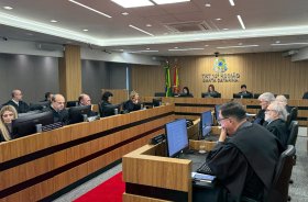 Trezes pessoas vestindo toga sentadas em fileiras de bancadas de madeira, em uma sala de julgamento