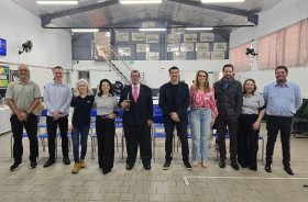 Seis homens e quatro mulheres posam para foto, lado a lado, dentro de uma sala ampla e com pé direito alto. Uma das pessoas, de terno, segura uma cuia de chimarrão