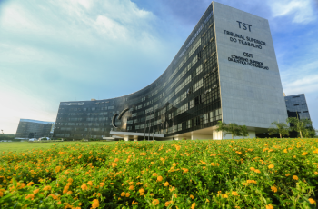 Fachada TST com jardim de pequenas flores na frente do prédio.  
