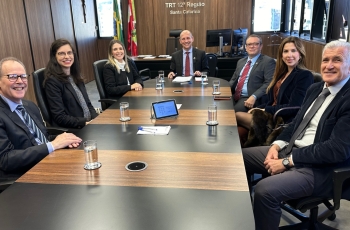 fotografia de uma reunião com seis pessoas vestidas formalmente e sorrindo ao redor de uma mesa