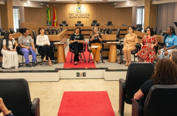 Oito mulheres sentadas em cadeiras, de frente para o público, em um evento formal