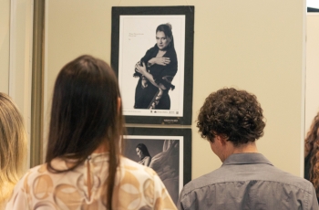 Duas pessoas, um homem e uma mulher, de costas, olhando para uma exposição fotográfica na qual as fotos são retratos em preto e branco de mulheres.