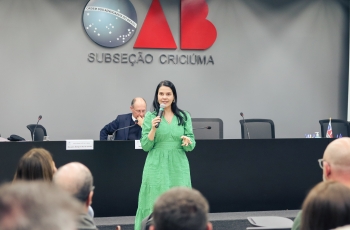 Uma mulher de vestido verde fala ao microfone para uma plateia 