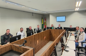Grupo de homens e duas mulheres posam para foto, sentados ao redor de uma mesa em uma sala de audiências