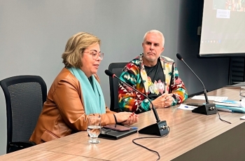Uma mulher e um homem estão sentados em um palco fazendo uma palestra
