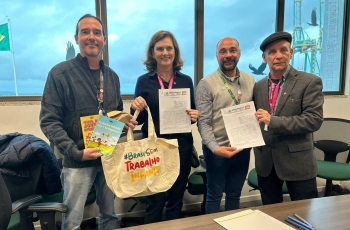 Quatro representantes posam com cartilhas e sacola da campanha Brasil Sem Trabalho Infantil após assinatura de parceria.