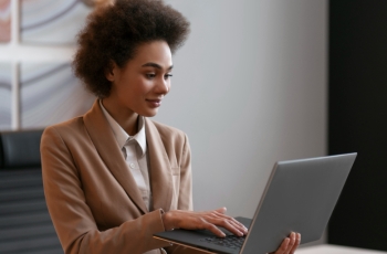 Fotografia ilustrativa de mulher negra vestida formalmente utilizando o notebook em um escritório