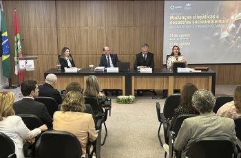 Mesa composta de quatro pessoas e público em primeiro plano assistindo palestra