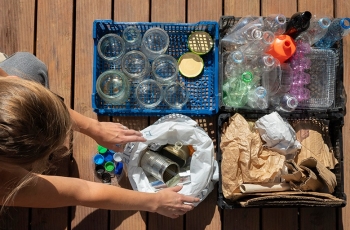 Fotografia ilustrativa em que pessoa separa resíduos recicláveis em caixas